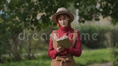 年轻迷人的红头发女人戴着帽子和毛衣在一个<strong>自然</strong>公园看书。 秋天<strong>凉</strong>爽的一天。